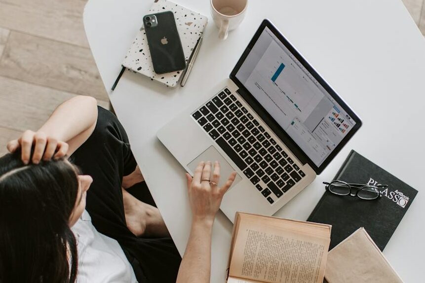 From above of young woman with long dark hair in casual clothes working at table and browsing netbook while sitting in modern workplace and touching hair