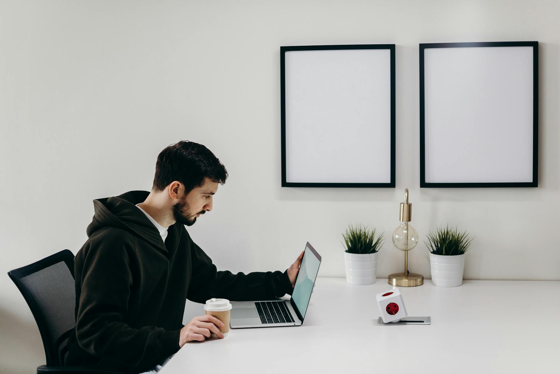 Young man in a hoodie works on a laptop in a modern, minimalist home office setup.