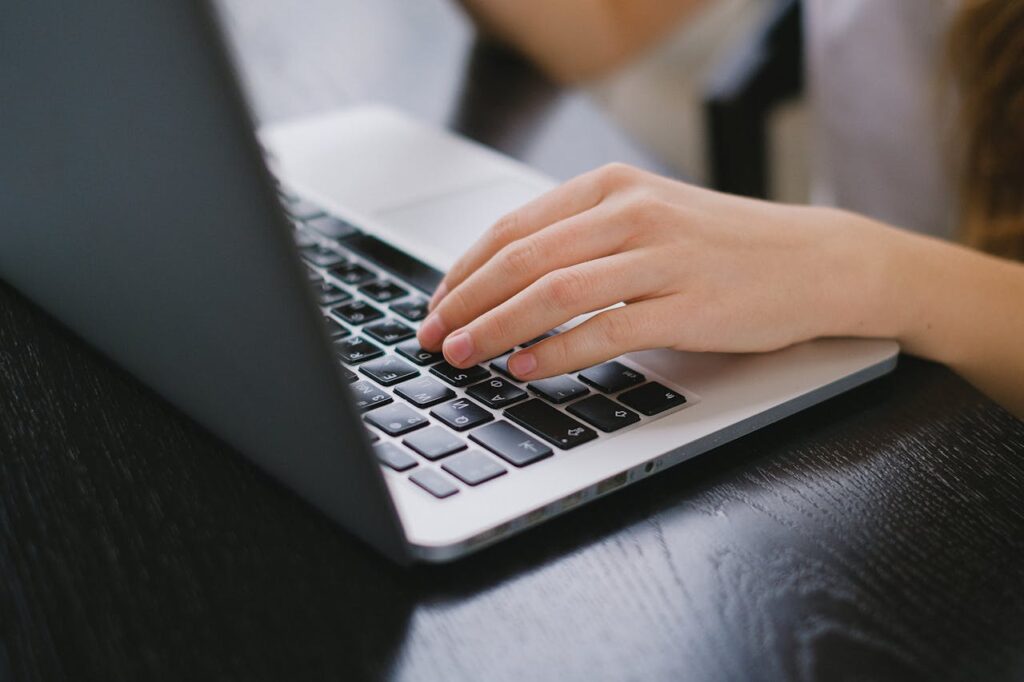 Close-up of a hand typing on a laptop keyboard placed on a wooden desk.